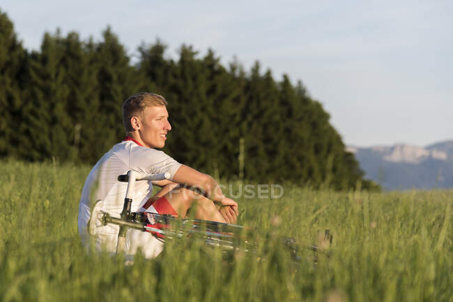Jovem ciclista masculino sentado no campo olhando para fora — Fotografia de Stock