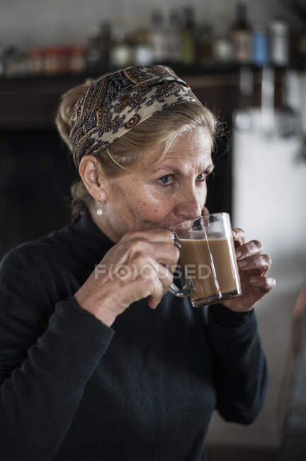 Blond haired senior woman drinking coffee in kitchen — Stock Photo