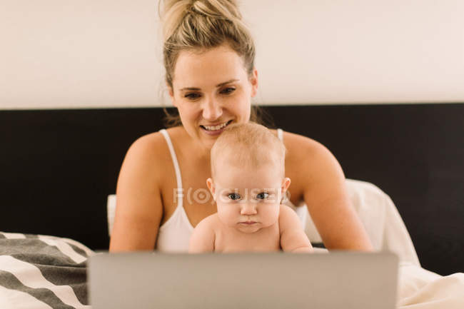 Дитяча дівчинка і мати сидять в ліжку з ноутбуком — стокове фото