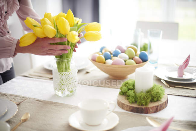 Imagem cortada da mulher que arranja tulipas amarelas na mesa de jantar da Páscoa — Fotografia de Stock