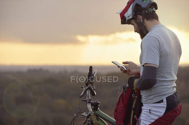 Чоловічий гірський велосипедист дивиться на смартфон — стокове фото