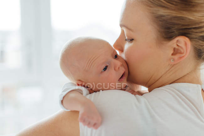 Jovem mulher beijando bebê filha na bochecha — Fotografia de Stock