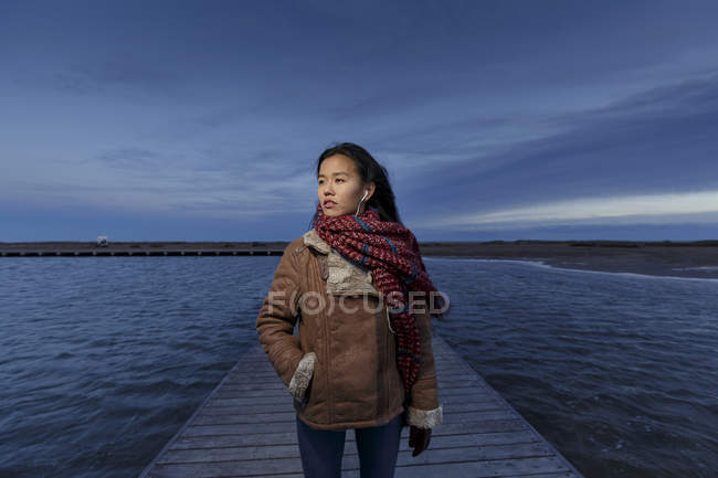 Junge Frau geht in der Abenddämmerung auf Seebrücke — Stockfoto