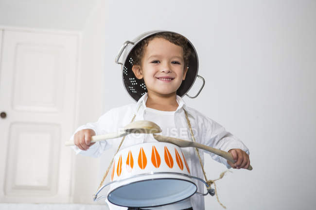 Мальчик барабанит в кастрюлю и улыбается в камеру — стоковое фото