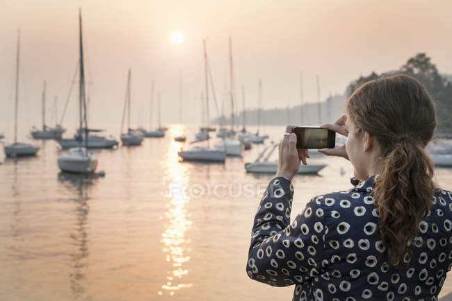 Visão traseira da mulher fotografando barcos ao pôr do sol, Lazise, Veneto, Itália, Europa — Fotografia de Stock