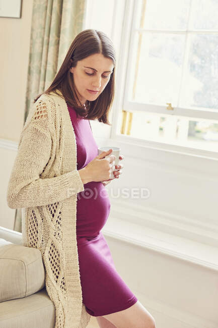 Pregnant woman leaning against sofa looking down — Stock Photo