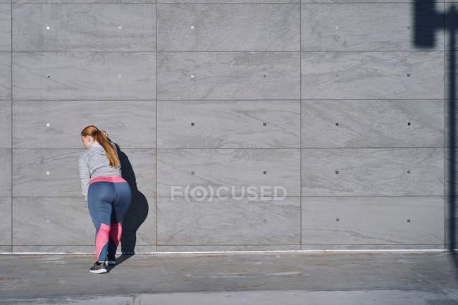 Curvaceous young woman doing wall push ups — Stock Photo