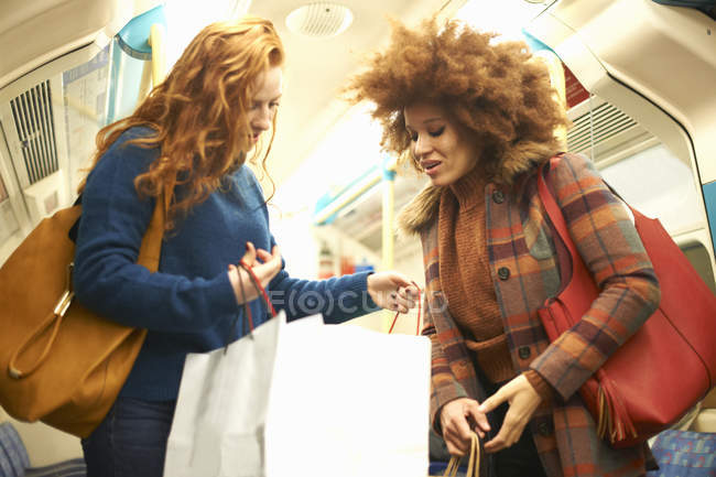 Two young women on train looking in shopping bag — Stock Photo