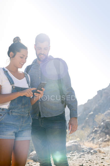 Junges Wanderpaar blickt im sonnenbeschienenen Tal auf das Smartphone, Las Palmas, Kanarische Inseln, Spanien — Stockfoto