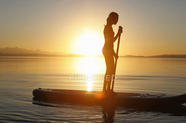 Rapariga remo embarque na água, ao pôr do sol — Fotografia de Stock
