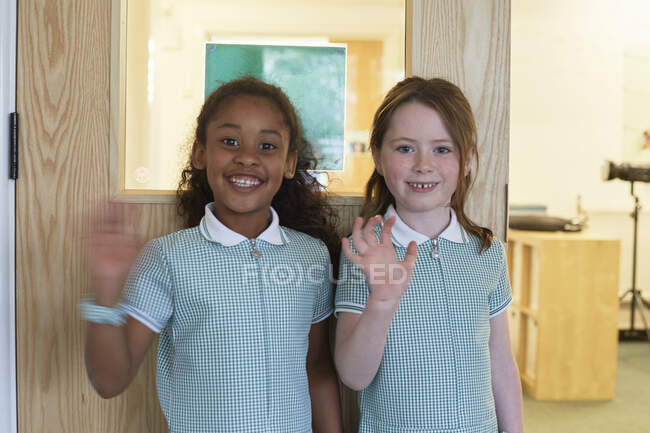 Portrait de deux écolières agitant le bras à l'école primaire — Photo de stock