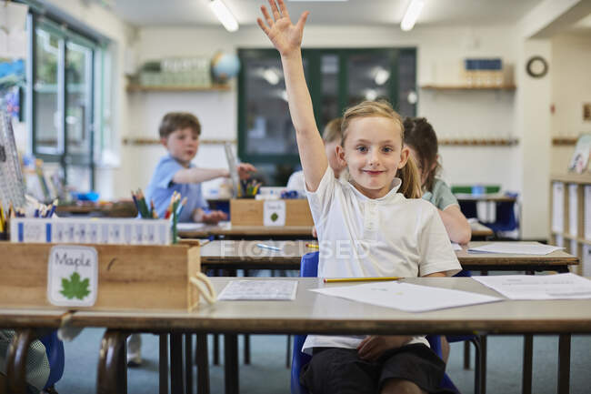 Schoolgirl with hand raised in classroom at primary school — Stock Photo