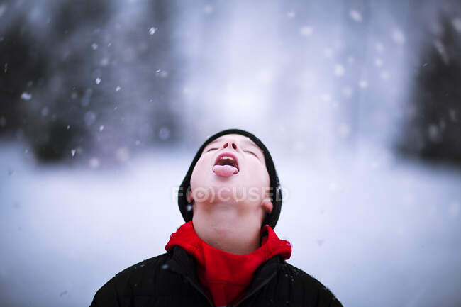 Porträt eines Jungen, der fallenden Schnee auf der Zunge fängt — Stockfoto