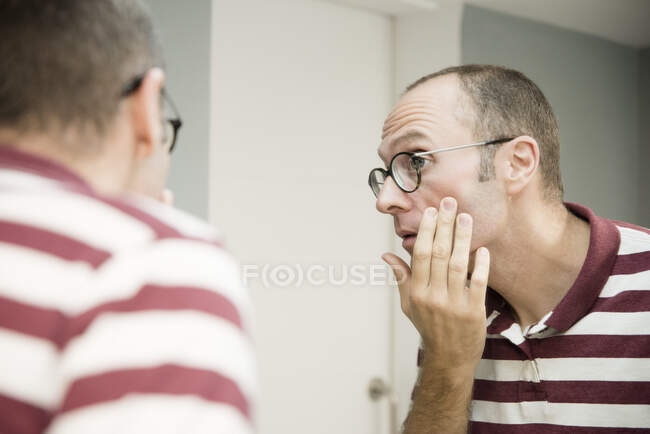 Через плечо вид зрелого мужчины, смотрящего на свое лицо в зеркало ванной — стоковое фото