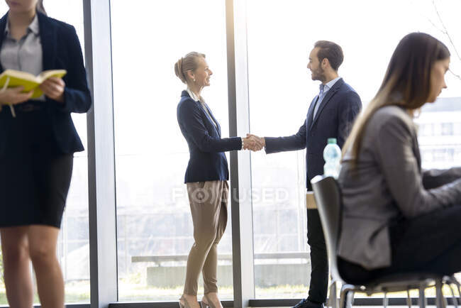 Femme d'affaires et homme serrant la main par la fenêtre du bureau — Photo de stock