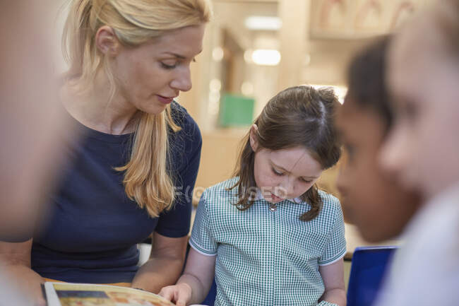 Teacher with schoolgirls reading storybook in classroom at primary school — Stock Photo