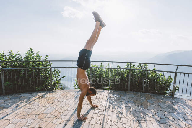 Молодой человек делает стойку на руках на смотровой площадке, озеро Комо, Ломбардия, Италия — стоковое фото