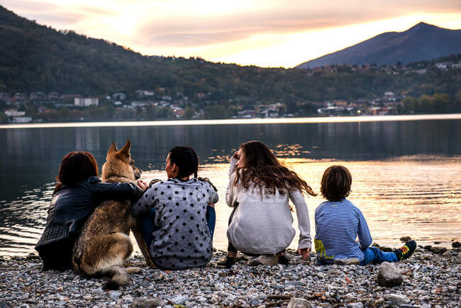 Rückansicht eines Jungen mit Familie und Hund am Fluss in der Dämmerung, Vercurago, Lombardei, Italien — Stockfoto