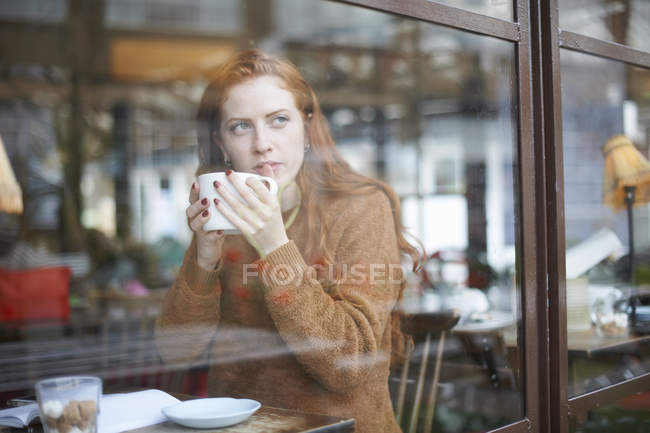 Vista através da janela da mulher na xícara de café segurando — Fotografia de Stock