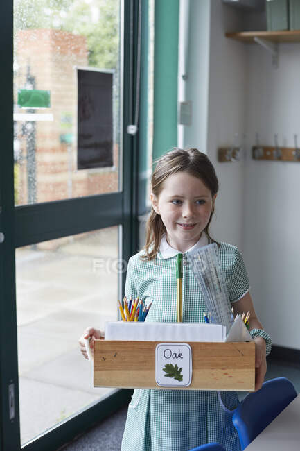 Schülerin trägt Schachtel mit Bleistiften im Klassenzimmer der Grundschule — Stockfoto
