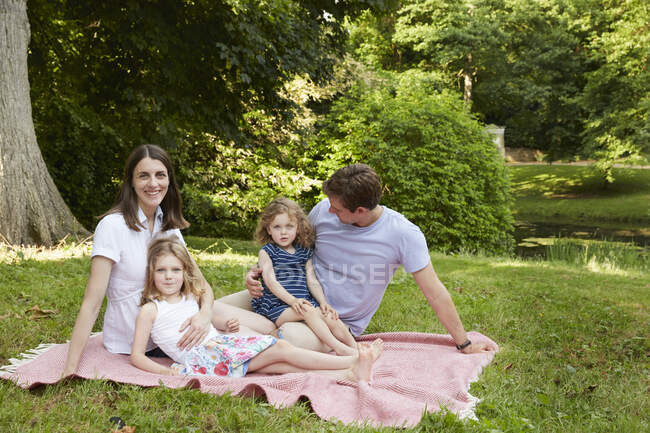 Портрет родителей среднего возраста и двух дочерей на одеяле для пикника в парке — стоковое фото