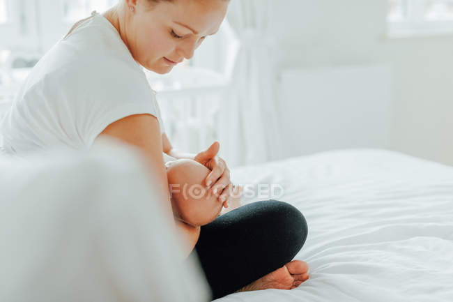 Jovem mulher sentada na cama e embalando bebê filha — Fotografia de Stock