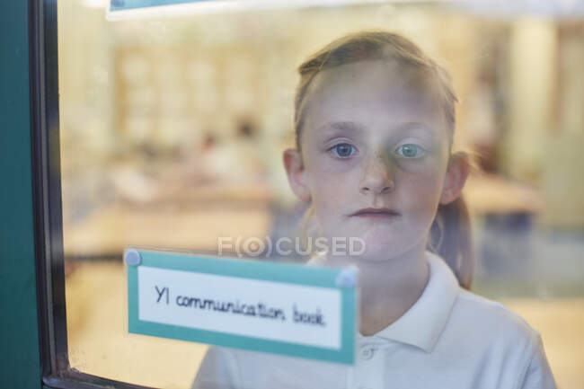 Portrait of schoolgirl looking through classroom window at primary school — Stock Photo