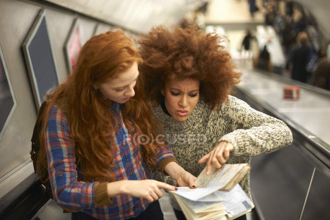 Two young women on escalator looking at map — Stock Photo