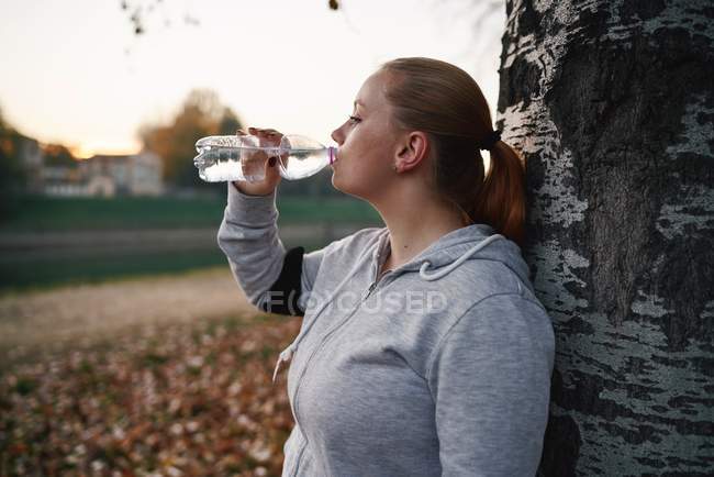 Formation de jeunes femmes courbes et eau potable en bouteille dans le parc — Photo de stock
