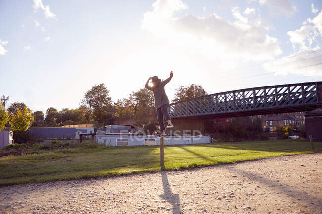 Frau balanciert auf Pfosten am Kanal, Brücke im Hintergrund — Stockfoto