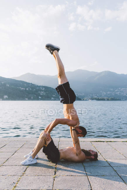 Two young men doing team handstand on waterfront, Lake Como, Lombardy, Italy — Stock Photo