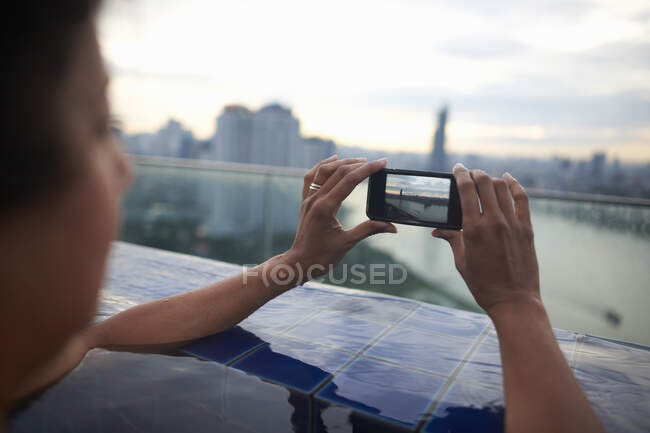 Woman in infinity pool taking photograph of view with smartphone, Bangkok, Krung Thep, Thailand, Asia — Stock Photo