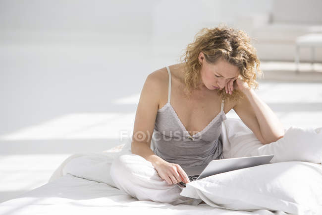 Femme assise sur le lit et utilisant un ordinateur portable — Photo de stock