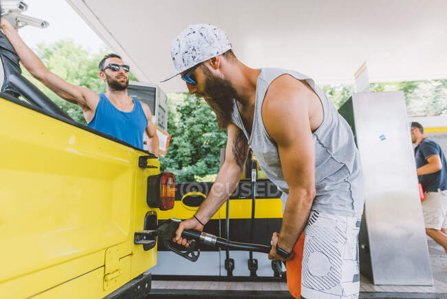 Jovem hipster macho que enche o veículo rodoviário no posto de gasolina em viagem de carro, Como, Lombardia, Itália — Fotografia de Stock