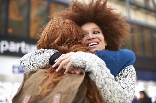 Dos mujeres jóvenes abrazándose en la estación de tren - foto de stock