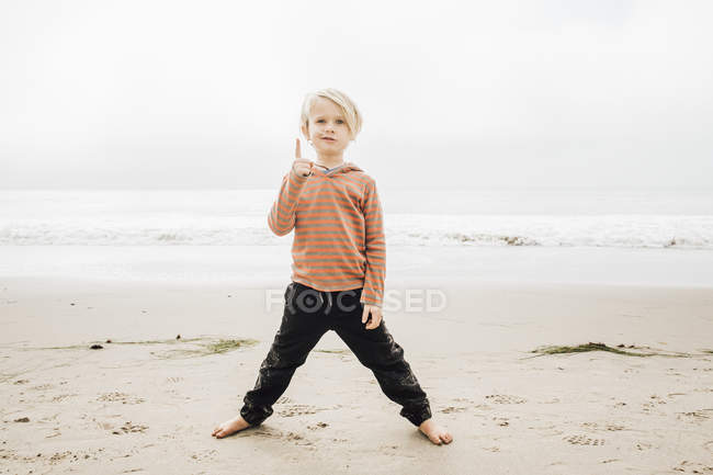 Portrait of young boy on beach with finger raised — Stock Photo