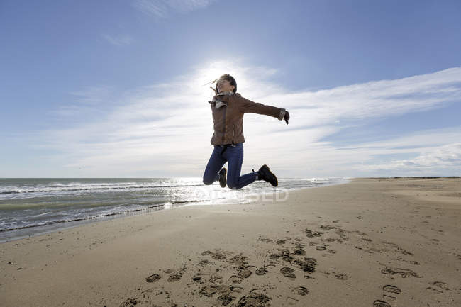 Young woman jumping mid air on beach — Stock Photo