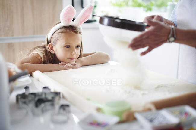Девочка смотрит, как бабушка просеивает муку для пасхальной выпечки — стоковое фото