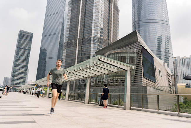 Hombre joven corriendo en el centro financiero de Shanghai, Shanghai, China - foto de stock