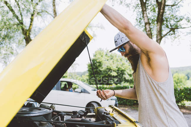 Young male lifting car hood on road — Stock Photo