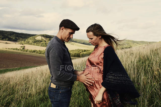 Romantic man with hands on pregnant wife stomach on hillside — Stock Photo