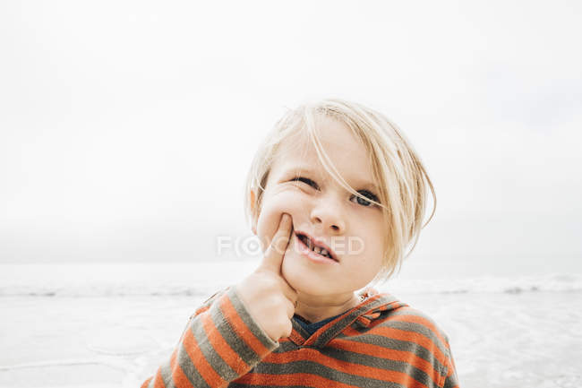 Portrait of young boy on beach making faces — Stock Photo