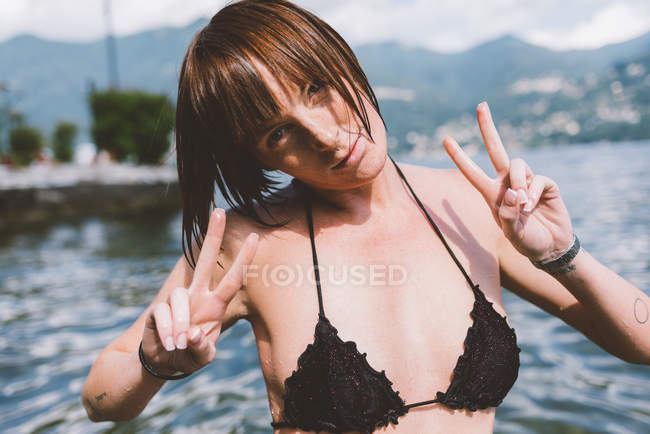 Portrait de jeune femme en haut de bikini faisant signe de paix au bord du lac de Côme, Lombardie, Italie — Photo de stock