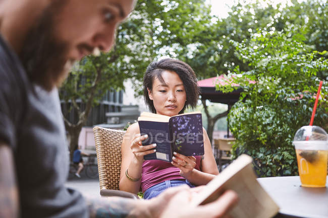 Розрахована на багато етнічні hipster пара читання книг на тротуарі кафе, Французька концесія Шанхай, Шанхай, Китай — стокове фото