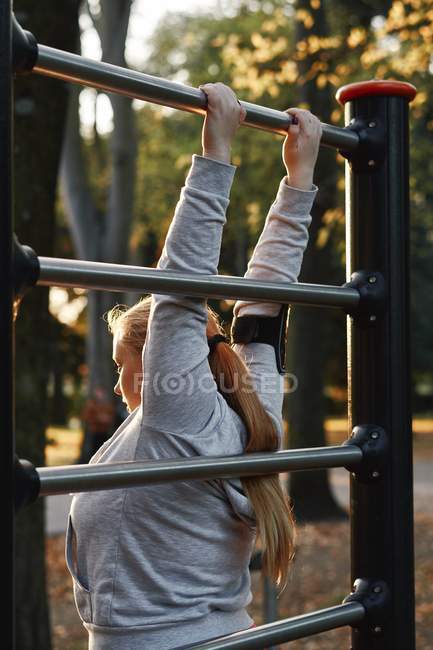 Курчавая молодая женщина тренируется и захватывает тренажер в парке — стоковое фото
