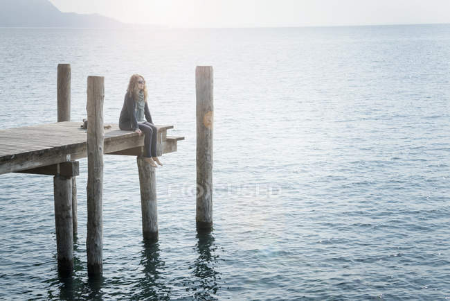 Женщина сидит на деревянном пирсе и смотрит в сторону — стоковое фото