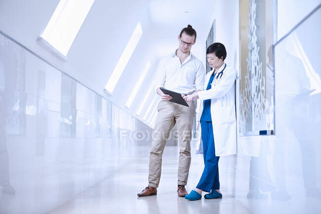 Medici in corridoio ospedaliero guardando tablet digitale — Foto stock