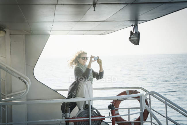 Femme en lunettes de soleil prenant des photos sur le ferry — Photo de stock