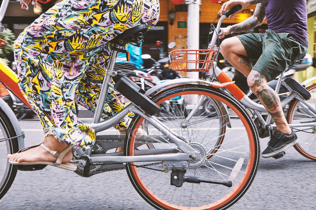Waist down view of multi ethnic hipster couple cycling along street, Shanghai French Concession, Shanghai, China — Stock Photo
