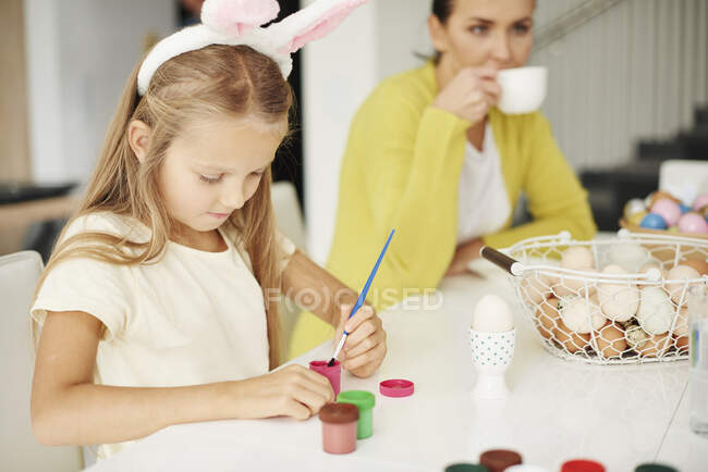 Дівчинка малює сире пасхальне яйце за столом. — стокове фото